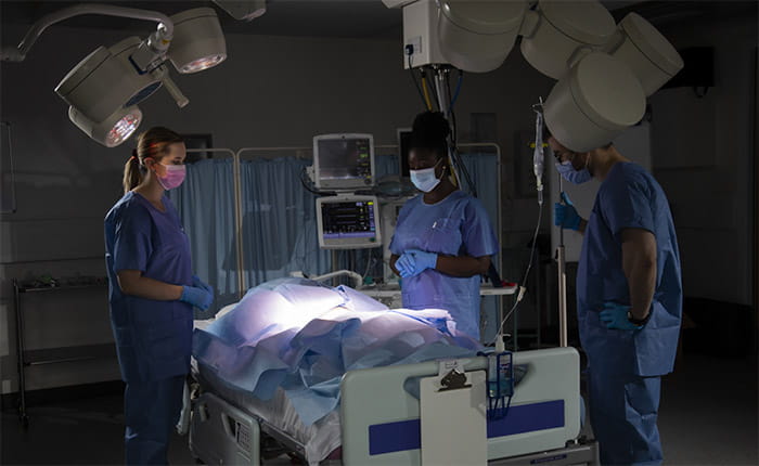 Three ODP students practicing on a dummy in a darkened skills lab