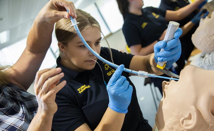 A Paramedic Science student practising intubating a dummy in the skills lab, with help from a tutor