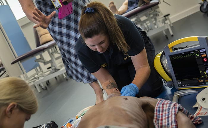 A Paramedic Science student practising on a dummy in the lab, with help from a tutor