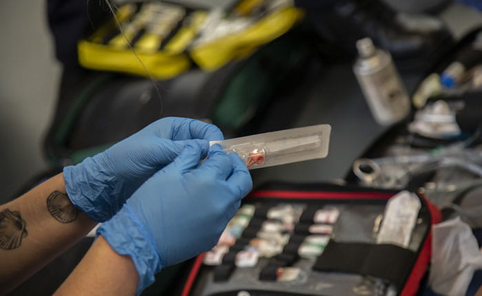 A pair of hands in blue surgical gloves, opening a package containing a medical item