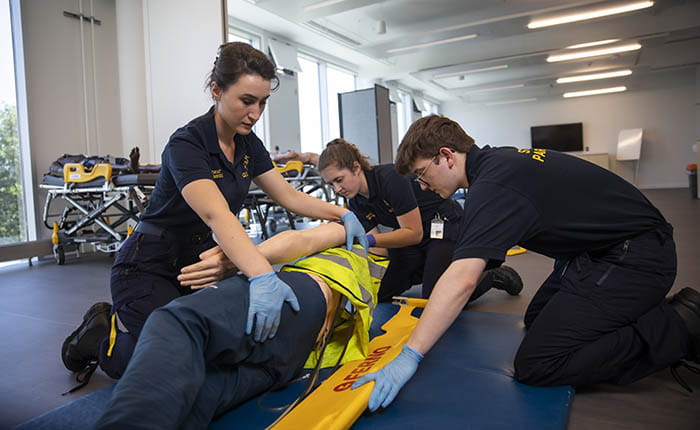 Three Paramedic Science students putting a dummy in the recovery position in the skills lab