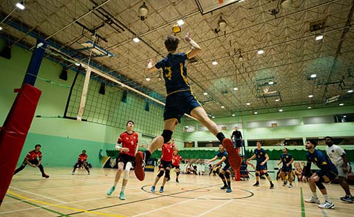 Two teams of students playing volleyball in the ARU sports hall, one jumping high in the air