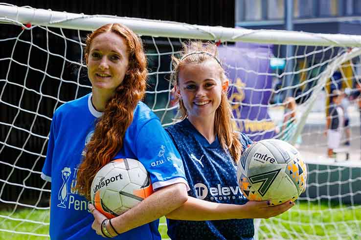 Two members of Peterborough Women's Football Club holding footballs in front of a goal