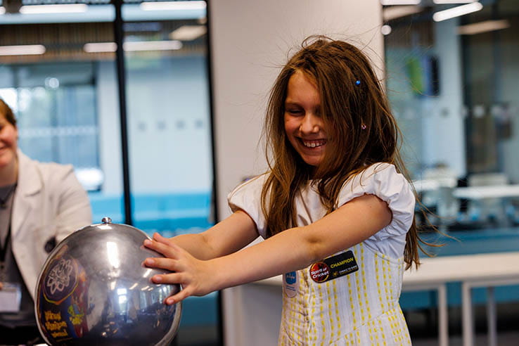 A young girl using a Van Der Graaf generator to make her hair stand on end