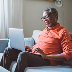 An older man sitting on a sofa, using a laptop