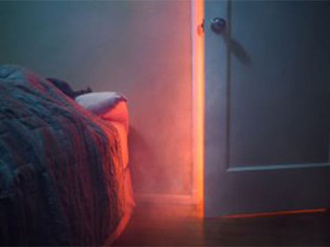 Smoke coming into a bedroom though an ajar door with the glow of flames behind it