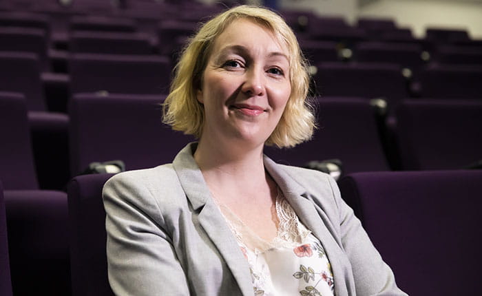 ARU student Sarah sitting in an empty lecture theatre with purple seats