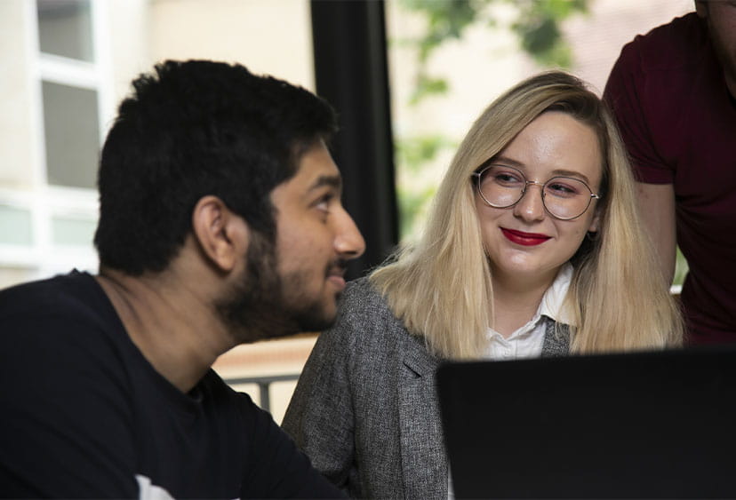 Two students looking at each other over a laptop