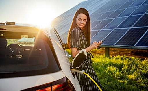 Close up of a woman holding a mobile phone charging an electric vehicle with cable