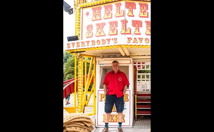 A smiling Showman standing in front of the entrance to a helter skelter
