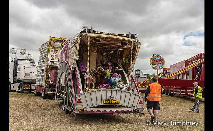 Back view of two showmen in hi-viz about to unpack fairground equipment from a trailer in a field