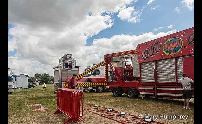 Two Showmen unpacking a tornado ride in a field, with trucks and other Showmen working in the background
