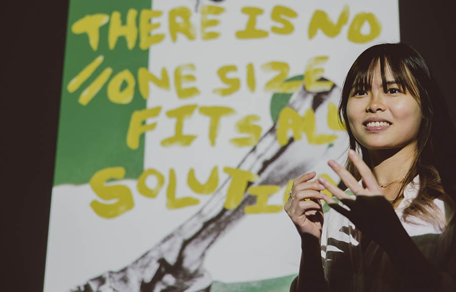 A student presenting in front of a screen that reads 'there is no "one size fits all" solution
