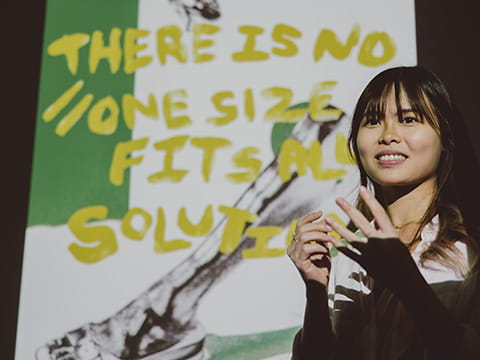 A student speaking in front of an artwork that says 'there is no "one size fits all" solution'