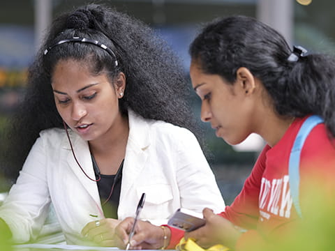Two students discussing whilst one writes on paper