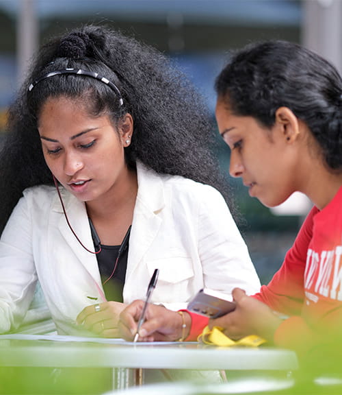 Two students discussing whilst one writes on paper