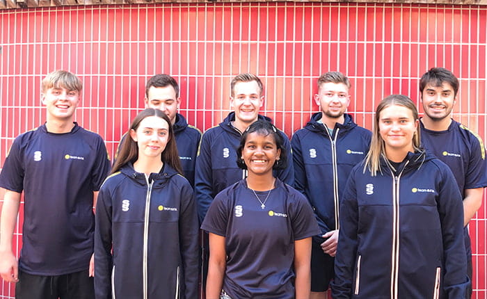 Eight ARU sport activators posed in two rows in front of a tiled wall