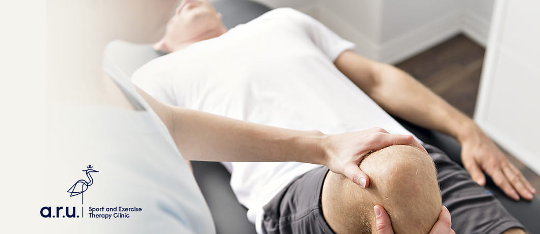 Partial view of a man receiving physiotherapy on his right knee on a massage table, with the ARU Sport and Exercise Therapy Clinic logo in the bottom left
