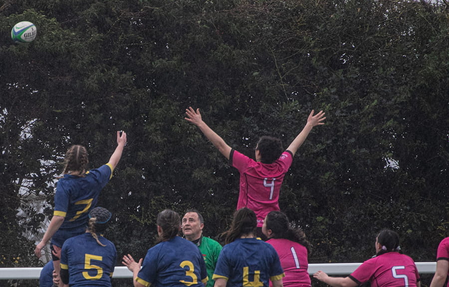 Back view of students playing rugby with a coach. The ball is in the air and two students are jumping up to catch it.