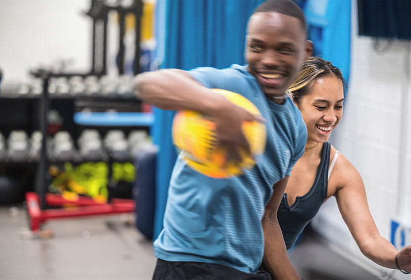 A male and female student play sport with a ball in gymnasium 