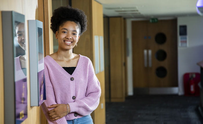 A student, smiling at the camera, in an office hallway