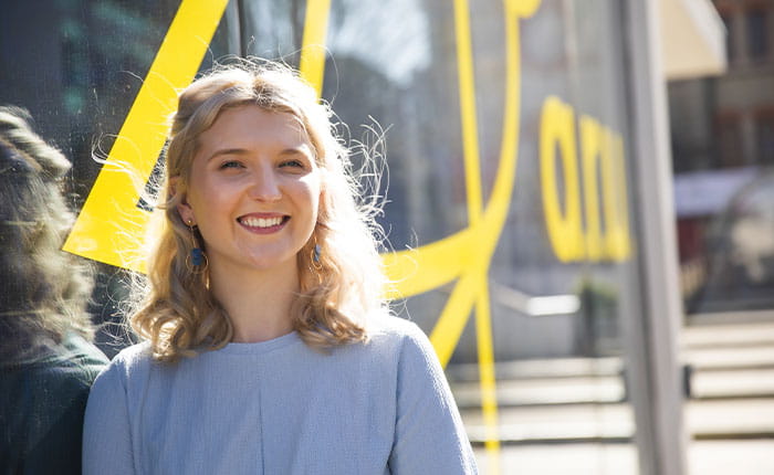 A smiling student standing outside the main entrance to the Cambridge campus