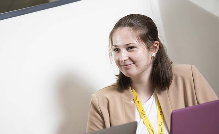 Student wearing a university lanyard and seated with laptop at desk