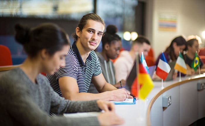 Students in a university classroom, at curved desk displaying flags of various countries
