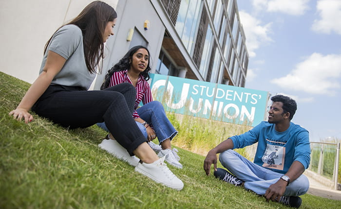 Three students sitting outside the Students' Union on ARU's Chelmsford campus