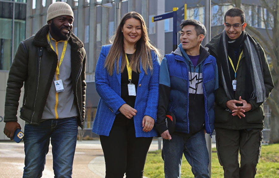 Four students walking on ARU Peterborough's campus, with University House behind them