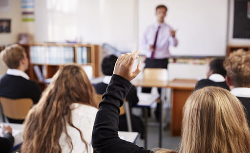A teacher (blurry due to distance/camera focus) teaching secondary school pupils in a classroom