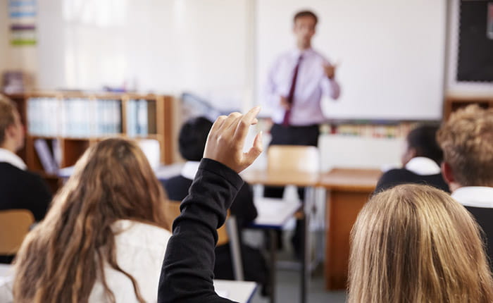 A teacher (blurry due to distance/camera focus) teaching secondary school pupils in a classroom
