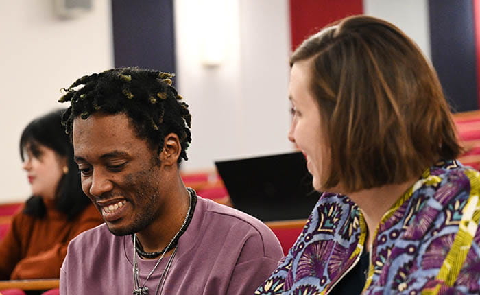 Two students sitting and talking in a lecture theatre, with another student visible in the background