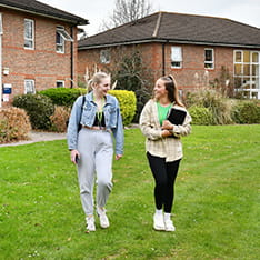 Two students walking on a lawn outside accommodation on the ARU Writtle campus