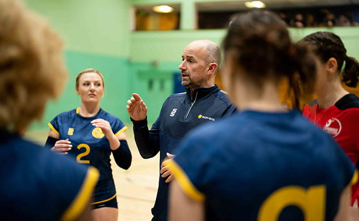 ARU Head Volleyball Coach Jean Jacquet talking to the women's team in a circle on the court