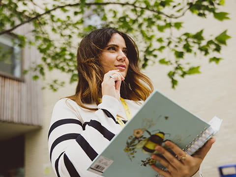 A student holding an open notebook and looking thoughtful