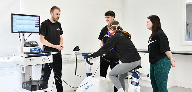 Four students - one using an exercise bike and the others monitoring performance - in a sport science centre