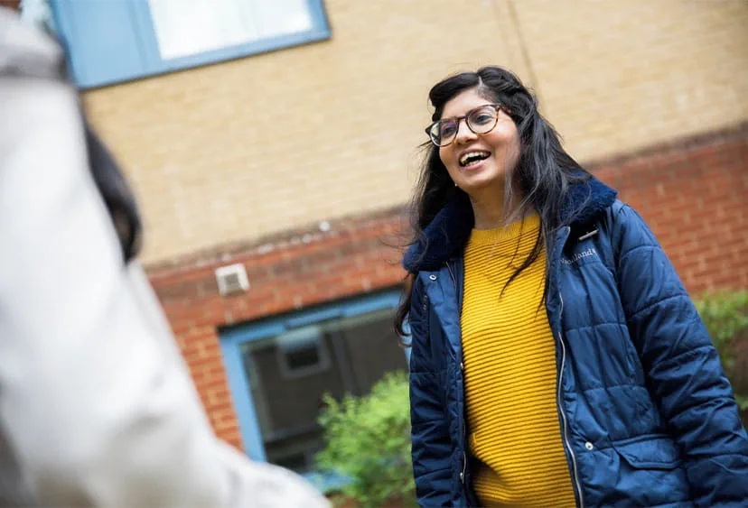 A student laughing with someone outside on campus 