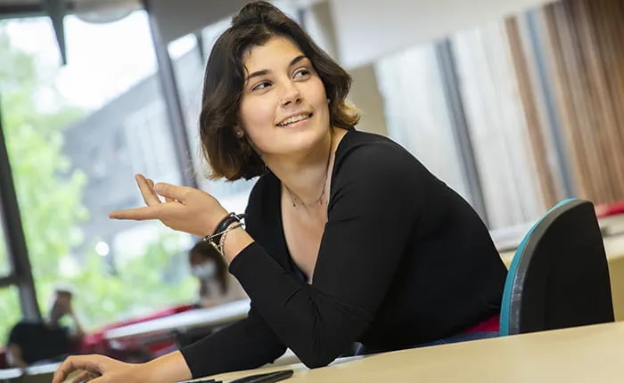 A female student working at a computer and speaking to someone out of shot