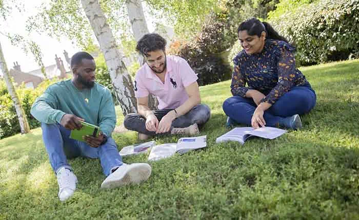 Three students sitting on grass with trees behind them