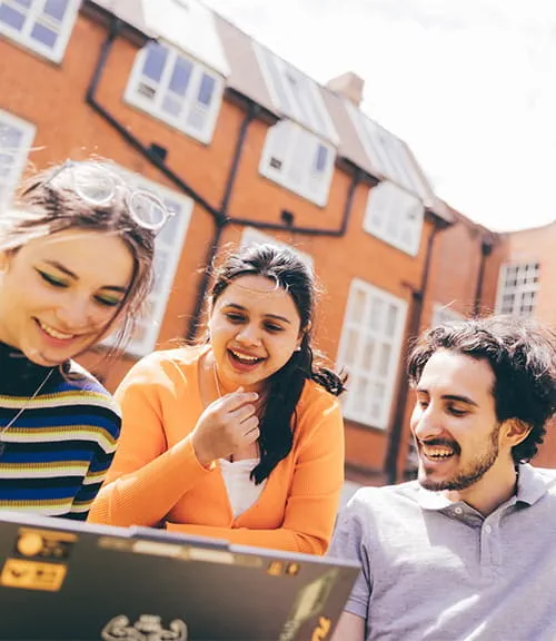 A group of students look at a laptop in the Cambridge campus grounds