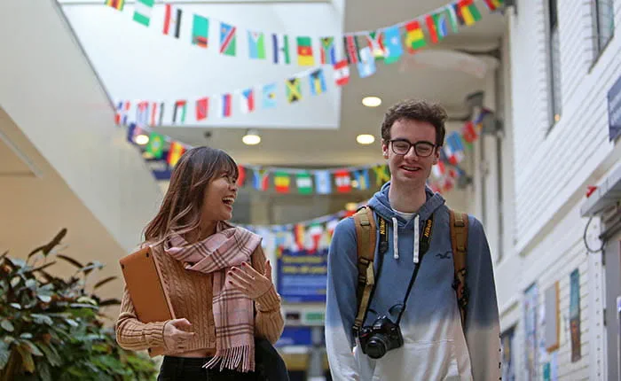 Two students walking and talking in a communal area with bunting of different flags hanging above them