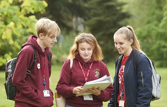 Three students standing in a group and looking at books