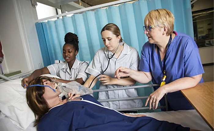 Student nurses practising putting breathing apparatus on and taking the pulse of a patient